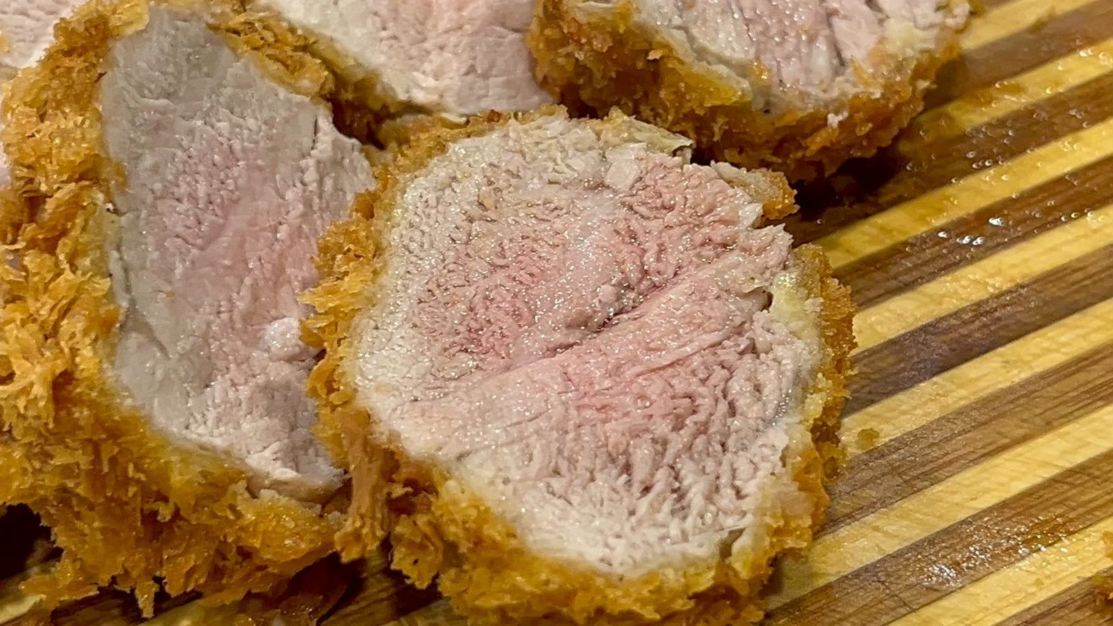 หมูสันในทอดสองรอบหั่นครึ่ง หน้าตัดสีชมพูระเรื่อ วางบนเขียงไม้ลายทาง