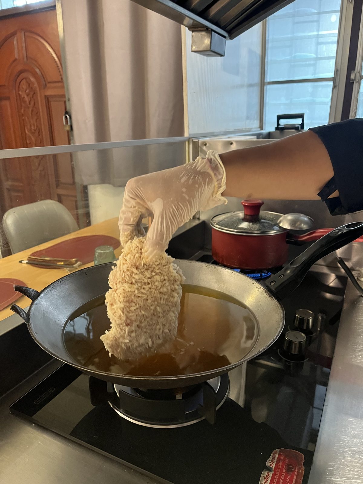 มือใส่ถุงมือกำลังหย่อนหมูชุบเกล็ดขนมปังลงกระทะน้ำมัน