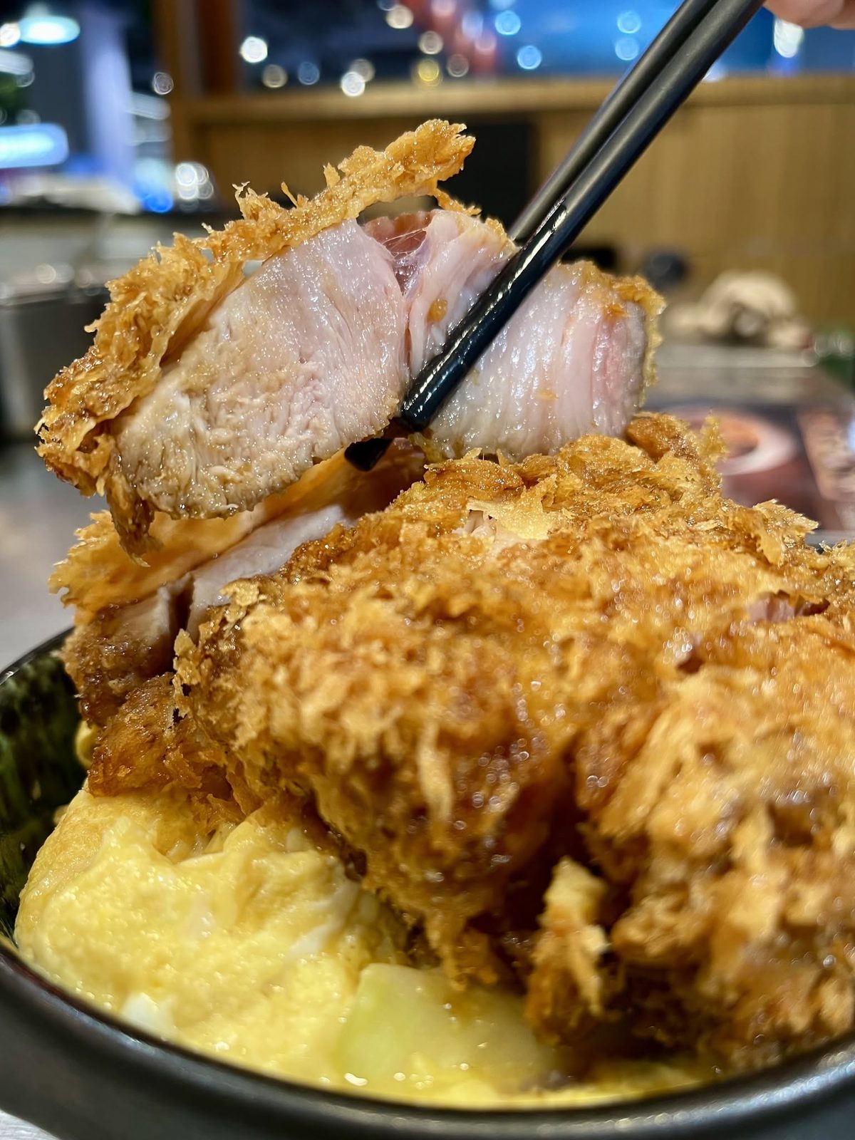 ตะเกียบคีบหมูทอดชิ้นหนาขึ้นจากชามคัตสึด้ง เห็นเนื้อด้านใน