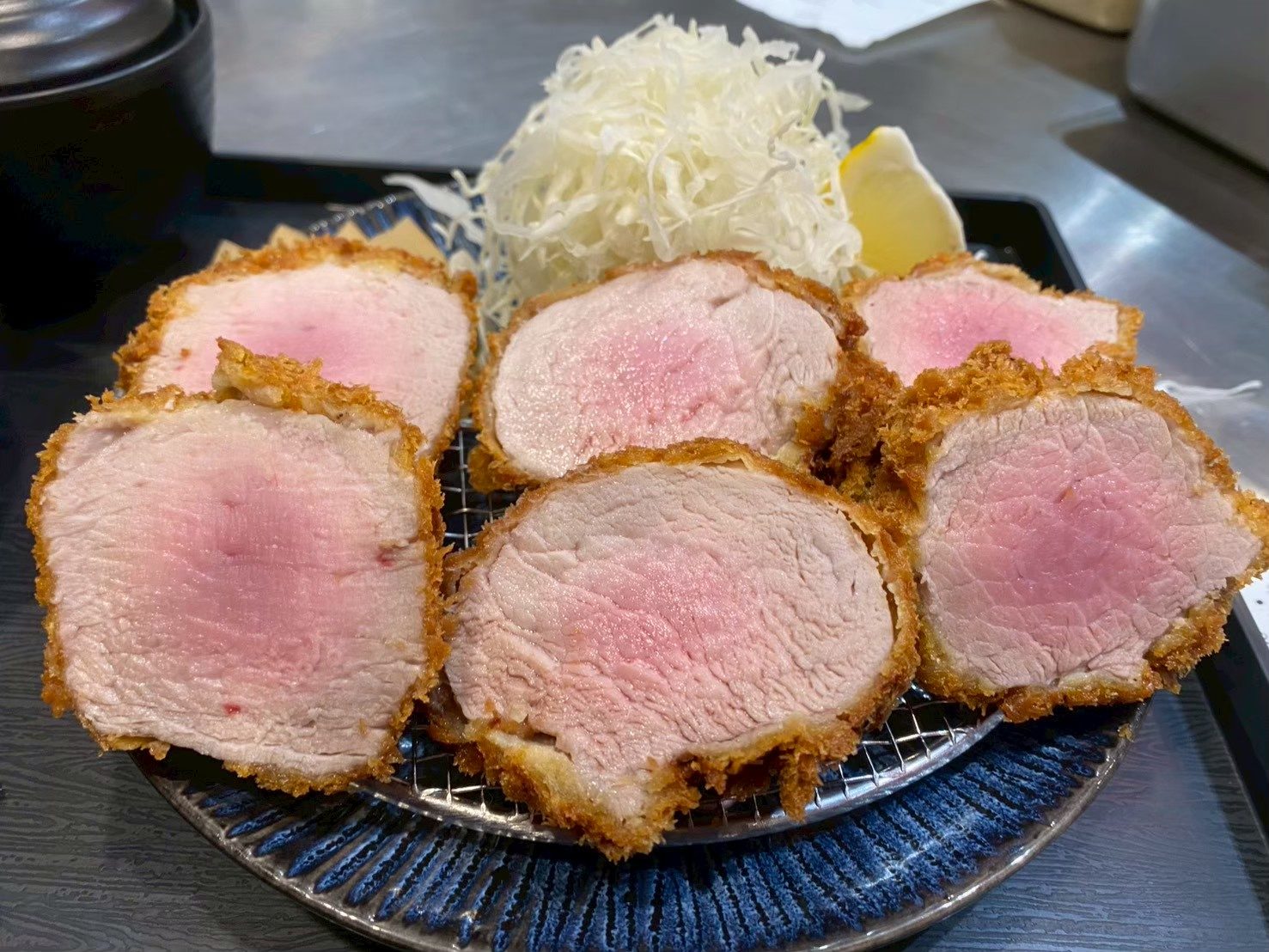 ทงคัตสึหมูสันในหั่นเป็นชิ้นกลม หน้าตัดสีชมพูระเรื่อ วางบนตะแกรงในจานสีน้ำเงิน