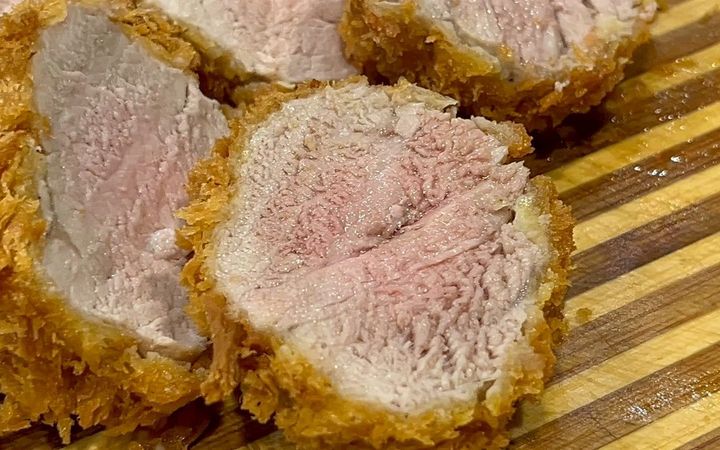 หมูสันในทอดสองรอบหั่นครึ่ง หน้าตัดสีชมพูระเรื่อ วางบนเขียงไม้ลายทาง