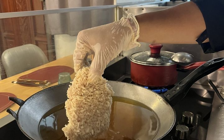 มือใส่ถุงมือหย่อนหมูชุบเกล็ดขนมปังลงกระทะน้ำมัน
