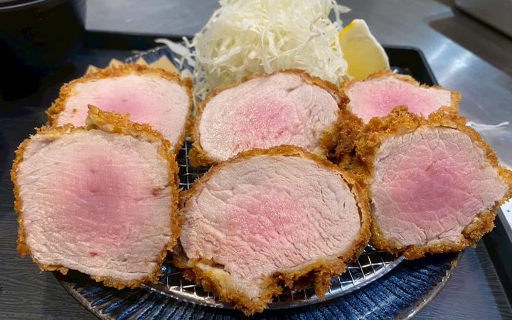 ทงคัตสึหมูสันในหั่นเป็นชิ้นกลม หน้าตัดสีชมพูระเรื่อ วางบนตะแกรงในจานสีน้ำเงิน